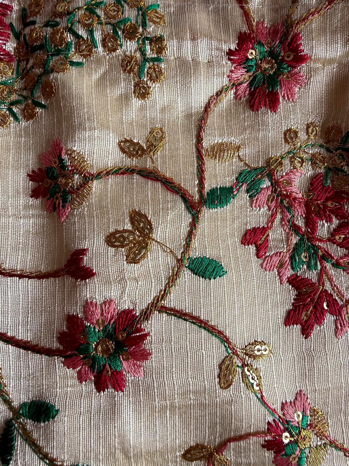 Close-up of floral embroidery in red, green, and gold on ivory fabric